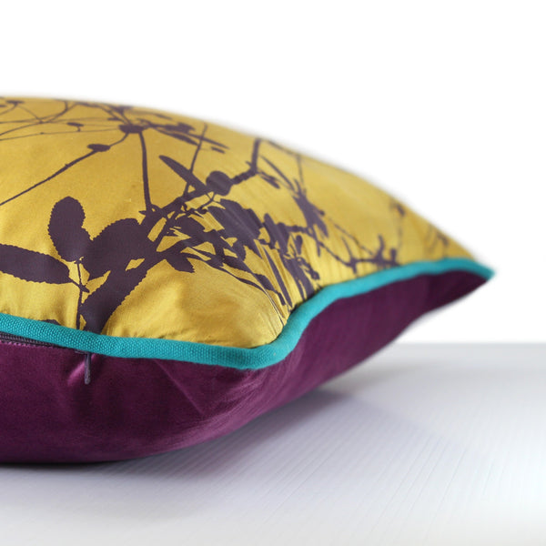 Side view of a vibrant gold silk cushion screen printed with sparse seed heads in an aubergine colour