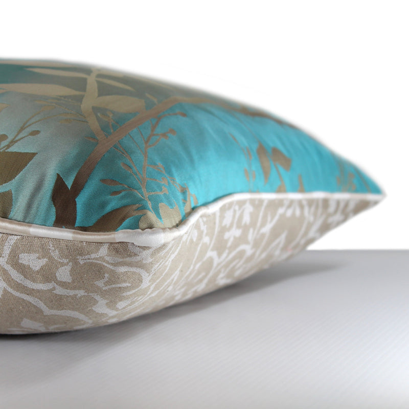Side view of a silk blend cushion in a luminous aqua ombre with sand coloured leaves and striped piping
