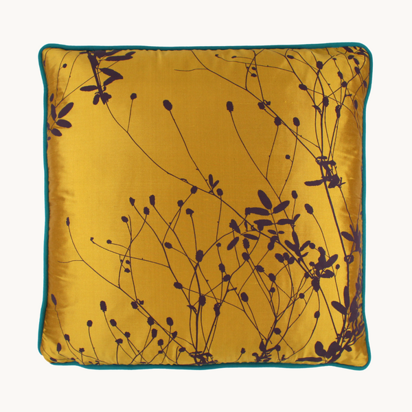 Photo of a vibrant gold silk cushion screen printed with sparse seed heads in an aubergine colour