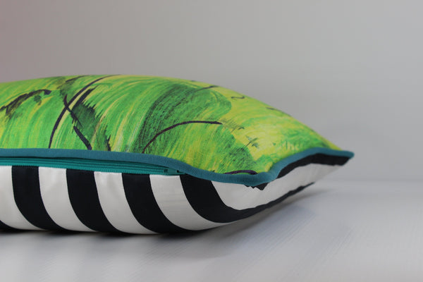Side view of a linen cushion in a painterly design with bright yellow, white, lime green and black with turquoise piping