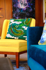 Photo of a colourful living room with a bright yellow chair that has an emerald coloured dragon cushion on it and artwork in the background.