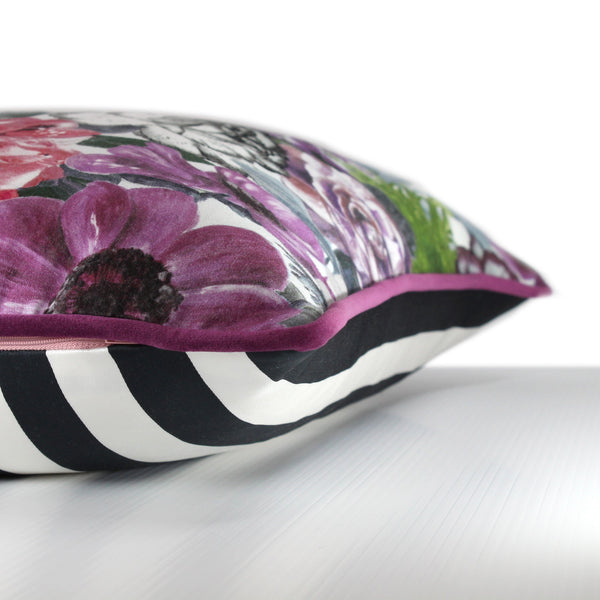 Side view of a vibrant floral cushion with a combination of painterly and digital blooms in purple, raspberry, lime, black and white with grape coloured velvet piping.