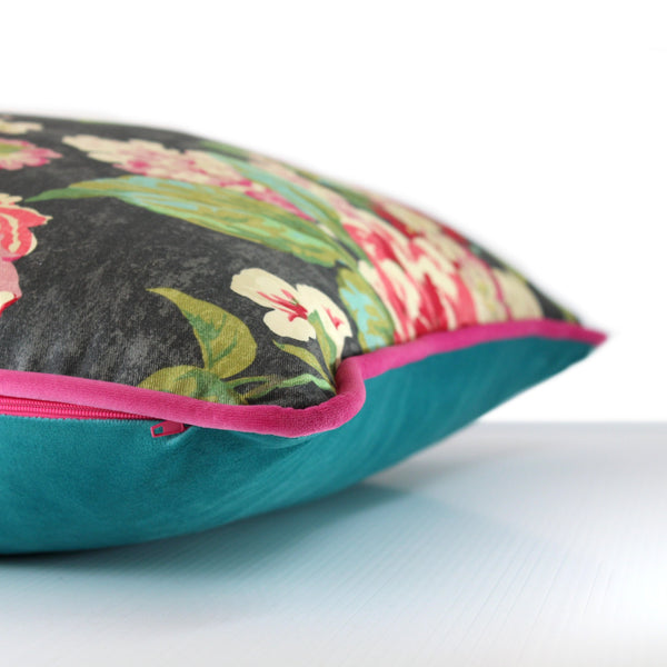 Side view of a cushion in a bright floral design with a charcoal base and bright pink, green and aqua roses and leaves and a hot pink velvet piping