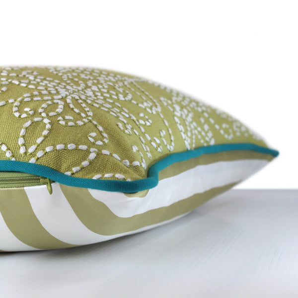 Side view of a chartreuse coloured cushion with white chunky scrolled embroidery detail and bright turquoise piping
