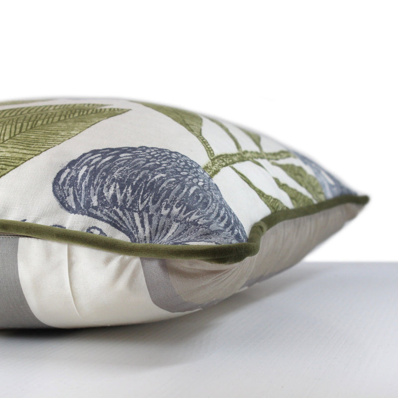 Side view of a cushion with a crisp white background and linear powdery blue proteas with green leaves