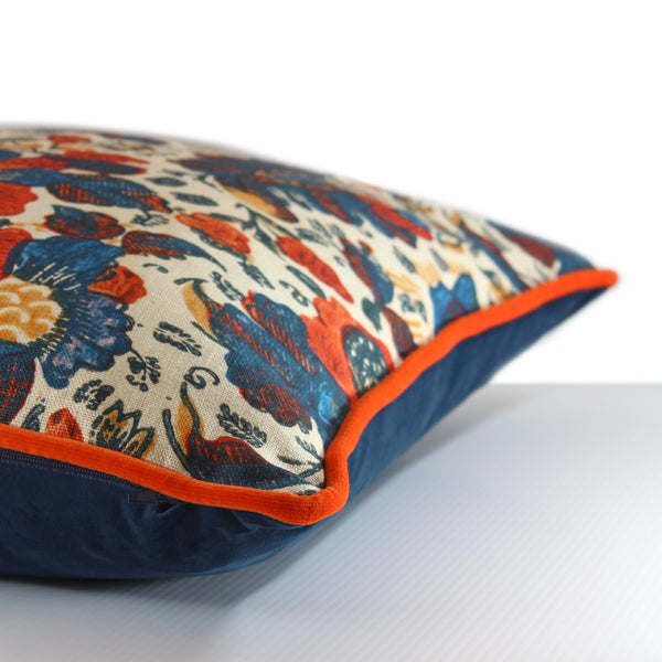 Side view of a cushion in a joyful combination of bright orange and navy blue in a painterly floral pattern with orange velvet piping