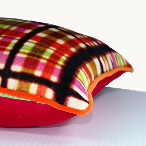 Sideshot of a square cushion in a very bright plaid design; oranges, pinks, lime green and licorice.