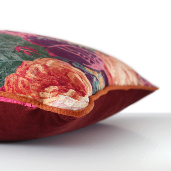 Side view of a luxurious large scale floral velvet cushion in rich colours of hot pink, orange, wine and greens with rust linen piping and a cinnamon velvet back