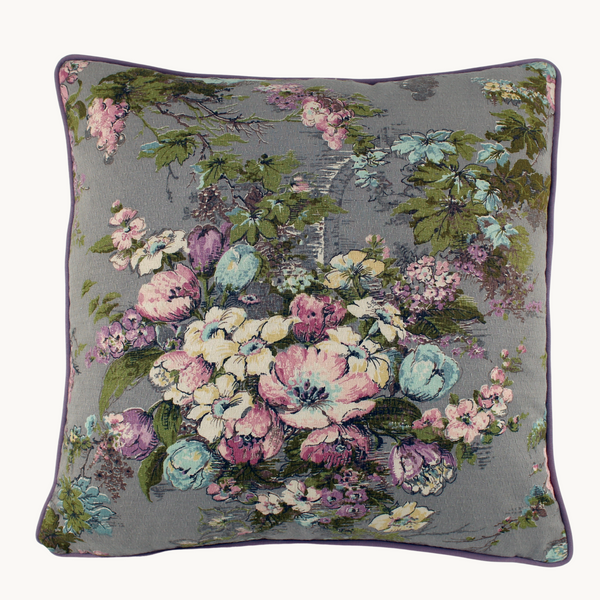Photo of a square cushion with a grey background and pink, blue and lilac flowers with vine like leaves.