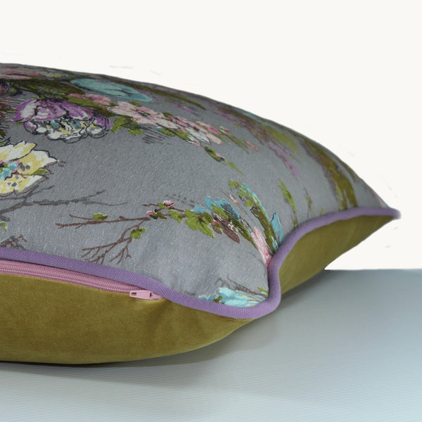 Side shot of a cushion with a grey background and pink, blue and lilac flowers and olive vine like leaves. 