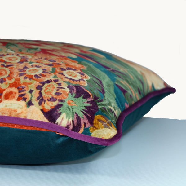 Sideshot of a vibrant velvet floral cushion in teal, orange, rust, aubergine and peach.